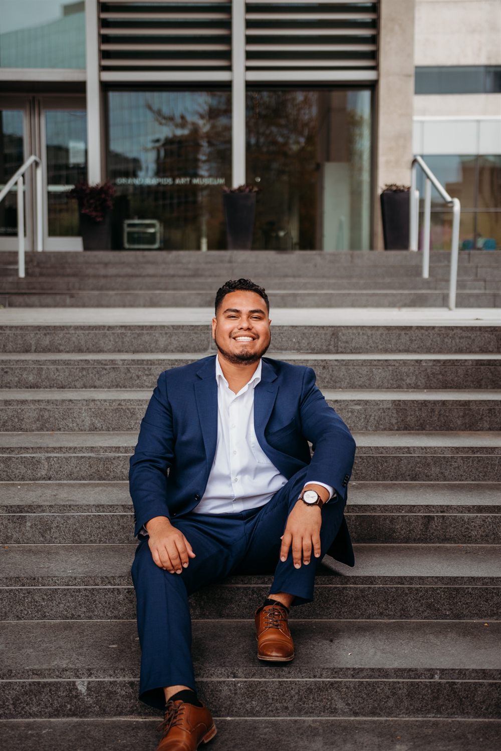Carlos Garcia, founder of Happy Health Benefits, sitting on the steps of the Grand Rapids Art Museum